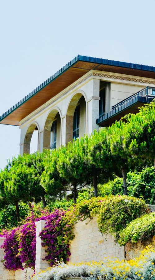 Stunning Mediterranean villa framed by vibrant greenery and florals under a clear sky.